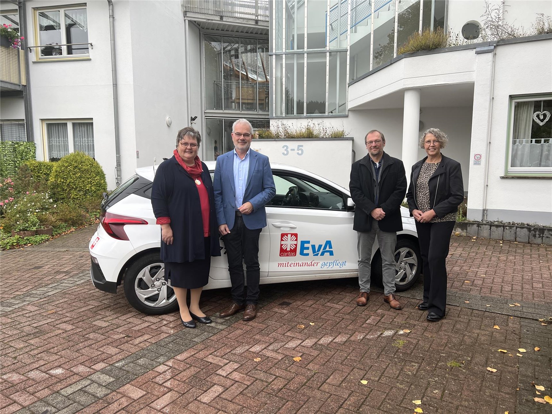Vier Personen stehen vor einem Dienstwagen der ambulanten Pflege, auf dem die beiden Logos der Caritas und Stiftung Evangelisches Altenheim Gemünd abgebildet sind: Ute Stolz (Vorstand Caritas), Malte Duisberg (Stiftung EvA), Pfarrer Christoph Ude (Vorstand EvA), Elisabeth Nosbers (Fachbereichsleitung Gesundheit und Pflege, Caritas Eifel)